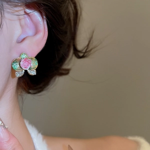 Detail view of floral enamel earrings with green petals and crystal accents on model