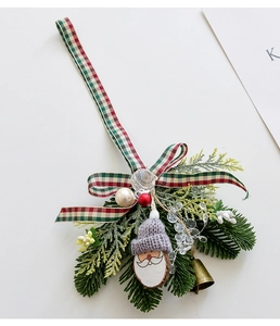 Detail of Christmas Santa ornament with pine needles, red plaid bow, and golden bell charms