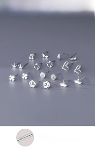 Macro detail of S999 silver studs featuring clover, crown and daisy shapes on grey background