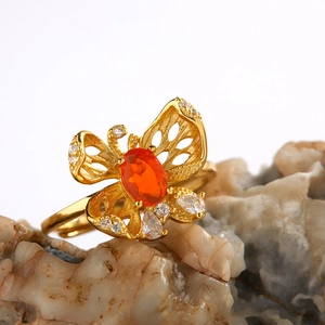 Golden butterfly ring with orange gemstone and white crystals on a natural stone base
