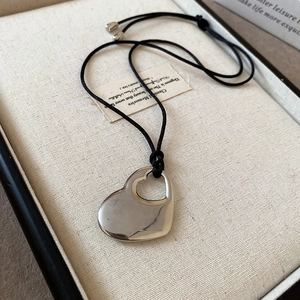 Detail of silver hollow heart pendant on black cord over a beige jewelry box