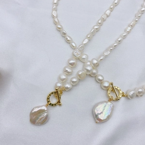 Detail of baroque pearl necklaces with gold T-bar clasps on white silk background