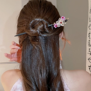 Detail of a floral wooden hair stick with pink blossoms and red berries in a bun