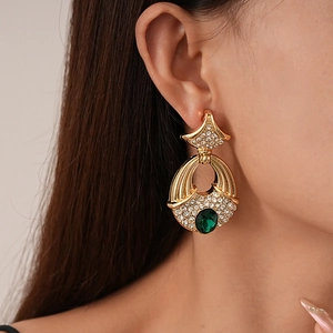 Gros plan de boucles d'oreilles dorées vintage avec émeraude verte et cristaux brillants