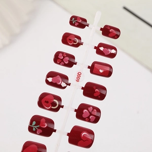 Short square red press-on nails with various heart patterns on a white holder