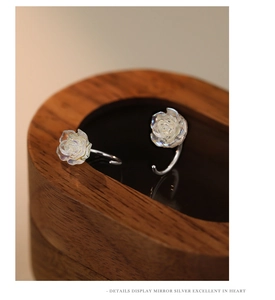 Macro shot of iridescent rose stud earring on dark wood display showing silver details