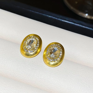 Macro shot of brushed gold oval stud earrings with diamond halo on leather background