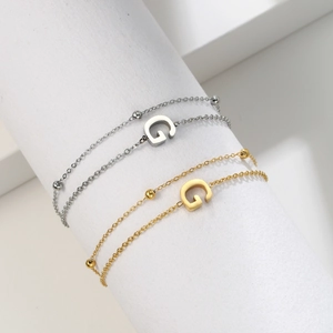Detail of minimalist stainless steel beaded bracelets with a letter G charm in gold and silver