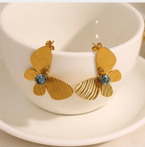 Detailed close-up of 18K gold butterfly earrings with blue turquoise inlay on white ceramic