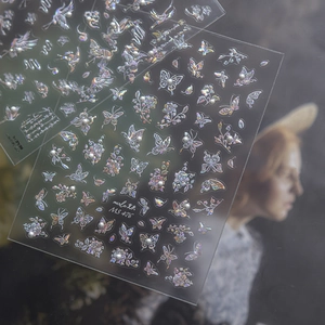 Close-up of holographic butterfly nail art stickers with pearl details on transparent sheets