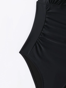 Close-up of ruched side detailing on black one-piece swimsuit for tummy control effect