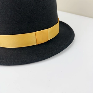 Detail of black wool felt top hat featuring a golden ribbed ribbon and bow decoration