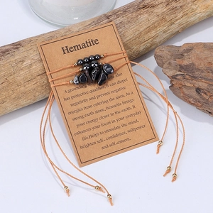 Detalle de pulsera de hematita hecha a mano con cordón encerado naranja en soporte de madera