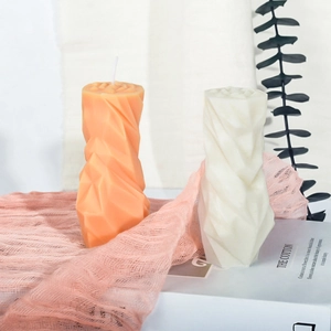 Geometrische origami geurkaarsen in oranje en crèmewit op een decoratieve stoffen achtergrond