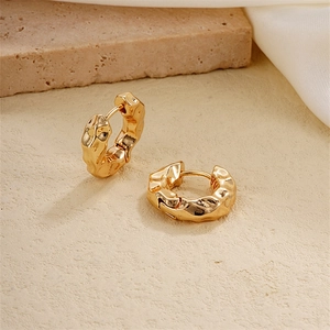 Detailed close-up of chunky gold huggie earrings with a textured lava finish on stone