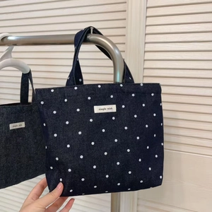 Detailed close-up of dark blue denim tote bag with white polka dots and simple wish label
