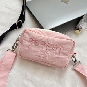 Detailed view of pink crossbody bag with bow embroidery, zipper, and wide strap on fabric