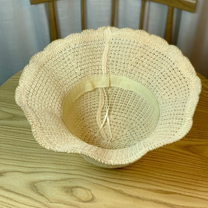 Detail of light beige crochet sun hat featuring wavy edges and adjustable inner drawstring