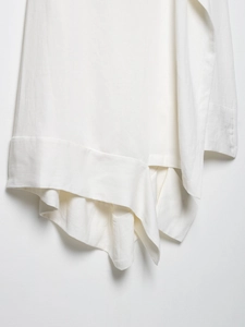 Detailed macro view of white linen-blend fabric texture and asymmetric layered hemline