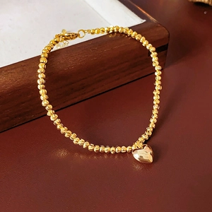 Detail of a golden beaded bracelet featuring a heart pendant on a wooden surface