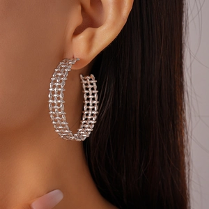 Close-up of a large silver hollow mesh C-shaped earring with woven texture