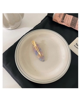 Detail of marble pattern acetate hair clip with golden metal clip in minimalist setting