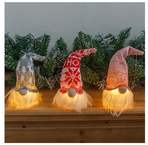 Three glowing Christmas gnomes with LED beards on a wooden surface with pine branches