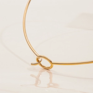 Close-up of a minimalist 18K gold-plated stainless steel necklace with a knot design