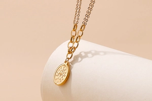 Detail of gold double-layer chain necklace with oval cross and M-letter embossed pendant