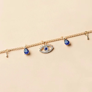 Collana dorata con occhio del diavolo, cristalli blu e pendenti su sfondo rosa