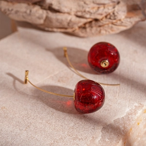 Macro detail of red resin cherry earrings with gold hooks and sparkling glitter finish