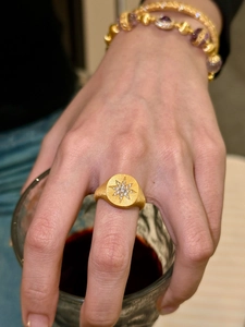 Detailed close-up of a gold-plated starburst signet ring with micro-set crystals