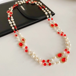 Detail of multi-layer vintage pearl necklace with red beads and golden metal accents