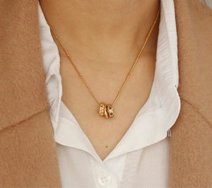 Detail of a gold-tone necklace with triple ring pendants and a green emerald zircon stone