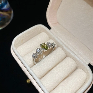 Detailed view of silver ring with green oval gemstone and pavé diamonds in jewelry box