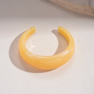 Detail of yellow translucent resin open bangle with white marble texture on beige stone