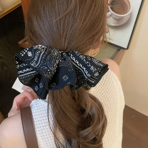 Détail d'un grand chouchou à nœud motif paisley noir et blanc porté sur une queue de cheval