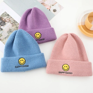 Close-up of knit texture and embroidered smiley face on winter beanies in various colors