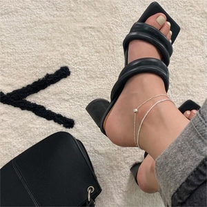 Detail of a minimalist silver beaded anklet styled with black square-toe heeled sandals