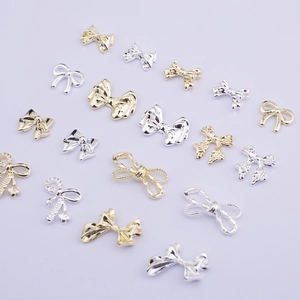 Assorted gold and silver 3D metal bow nail art charms displayed on light purple background