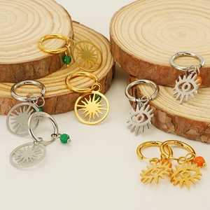 Détail de boucles d'oreilles créoles en acier avec breloques soleil et œil