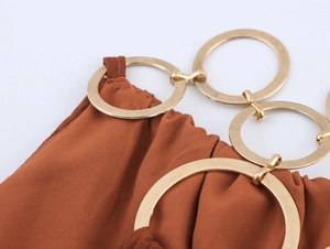 Makroansicht des braunen Faltenstoffs mit drei polierten goldenen Metallringen am Kleid