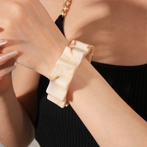 Close-up of wavy wide resin bracelet with cream marble texture and amber grain