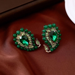 Gros plan de boucles d'oreilles vintage dorées avec cristaux verts sur satin sombre