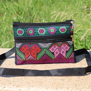 Detailed close-up of colorful floral embroidery and zippers on a black crossbody bag
