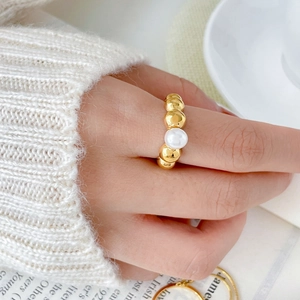 Detail of gold beaded ring with central white pearl on index finger against soft knit