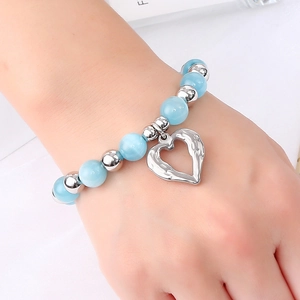 Detail of beaded bracelet with light blue cat eye stones and silver heart pendant on wrist