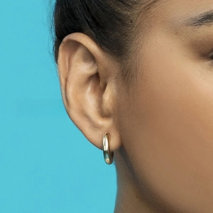 Close-up of a polished gold thick hoop earring on model against a bright blue background