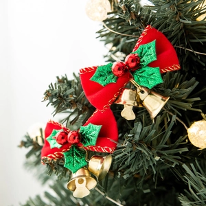 Red velvet Christmas bows with gold bells and holly berries hanging on a festive tree