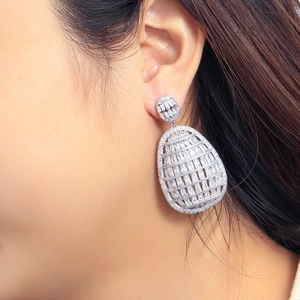 Detailed view of silver hollow drop earrings with clear zircons on model ear